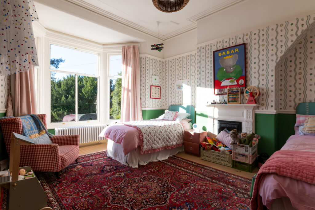 Children's bedroom decorated in 2025's Maximalist interior design trend, with patterned rug, wallpaper and curtains.