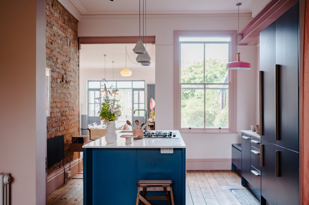 Kitchen with island and exposed brick wall, decorated in shades of pink, as per the 2025 interior design trend known as colour drenching. 
