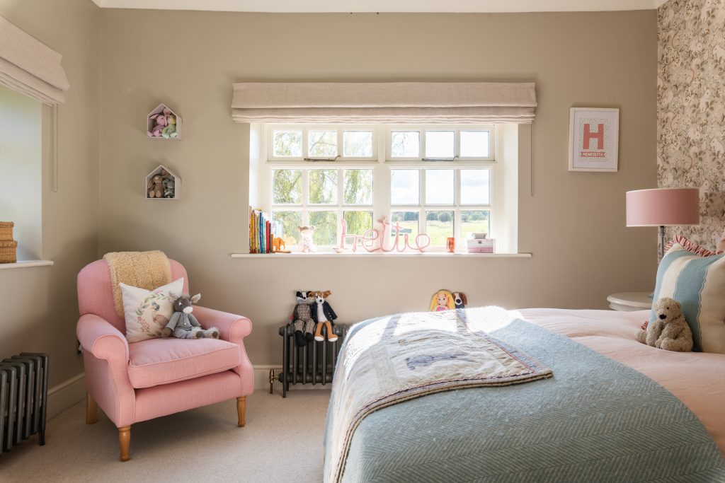 Bedroom with pale pink armchair and bed, decorated in 2025's 'warm neutrals' interior trend, with beige walls and carpet.