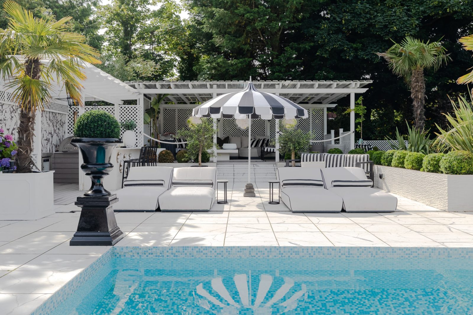 Ibiza style garden in Merseyside, with pool, white cushioned seating and a palm tree.