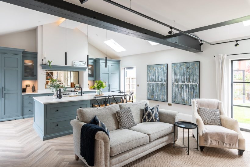 Large open plan living room and kitchen with a beam across the ceiling, a sofa in the foreground and a kitchen island behind it.