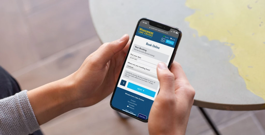 Windermere Lake Cruises booking screen on iPhone held by person at a table