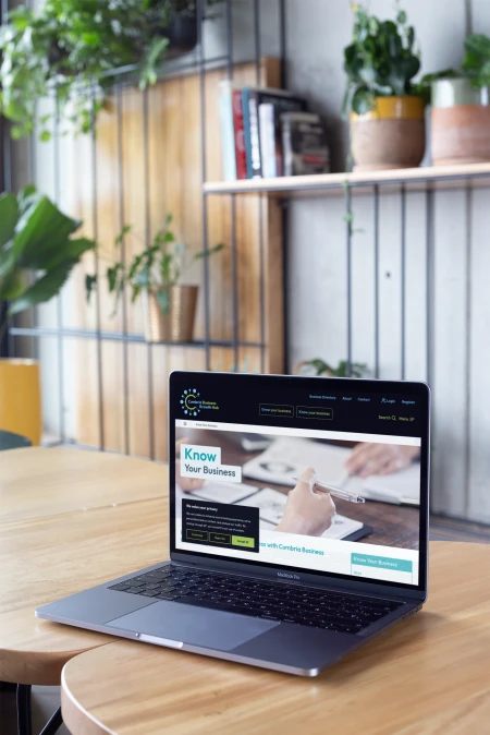 Mockup of a macbook standing on wooden tables near books and plants 21628