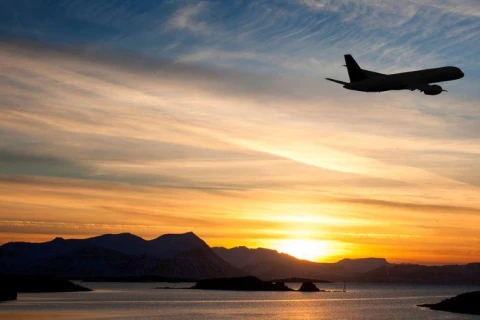 Aircraft taking off over coastal region at sunset