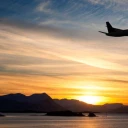 Aircraft taking off over coastal region at sunset