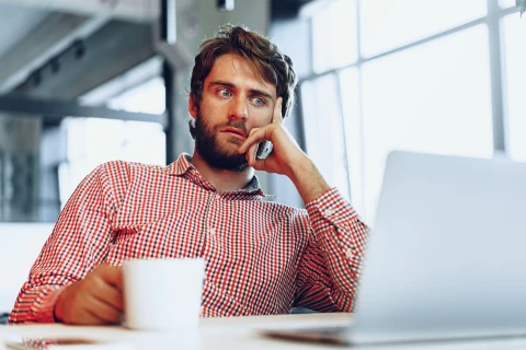 Man looking shocked while looking at a laptop while in an office