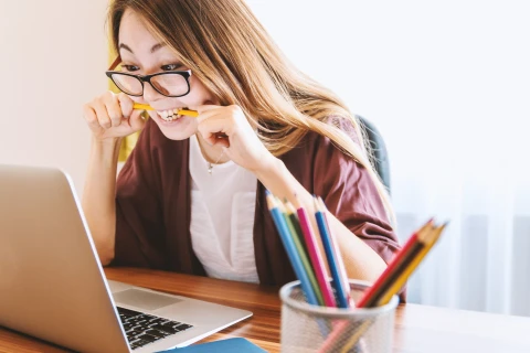 Woman biting pencil in front of computer
