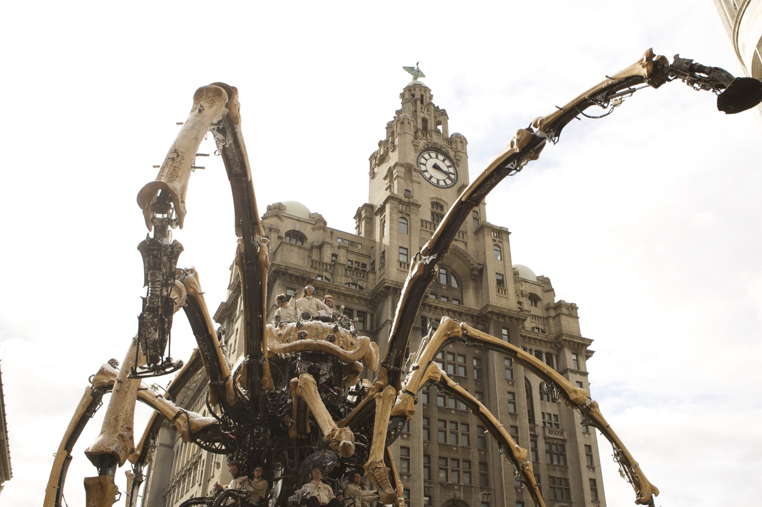 A giant mechanical spider with a large historical clocktower in the background. The shot is taken from below, making the spider look huge.