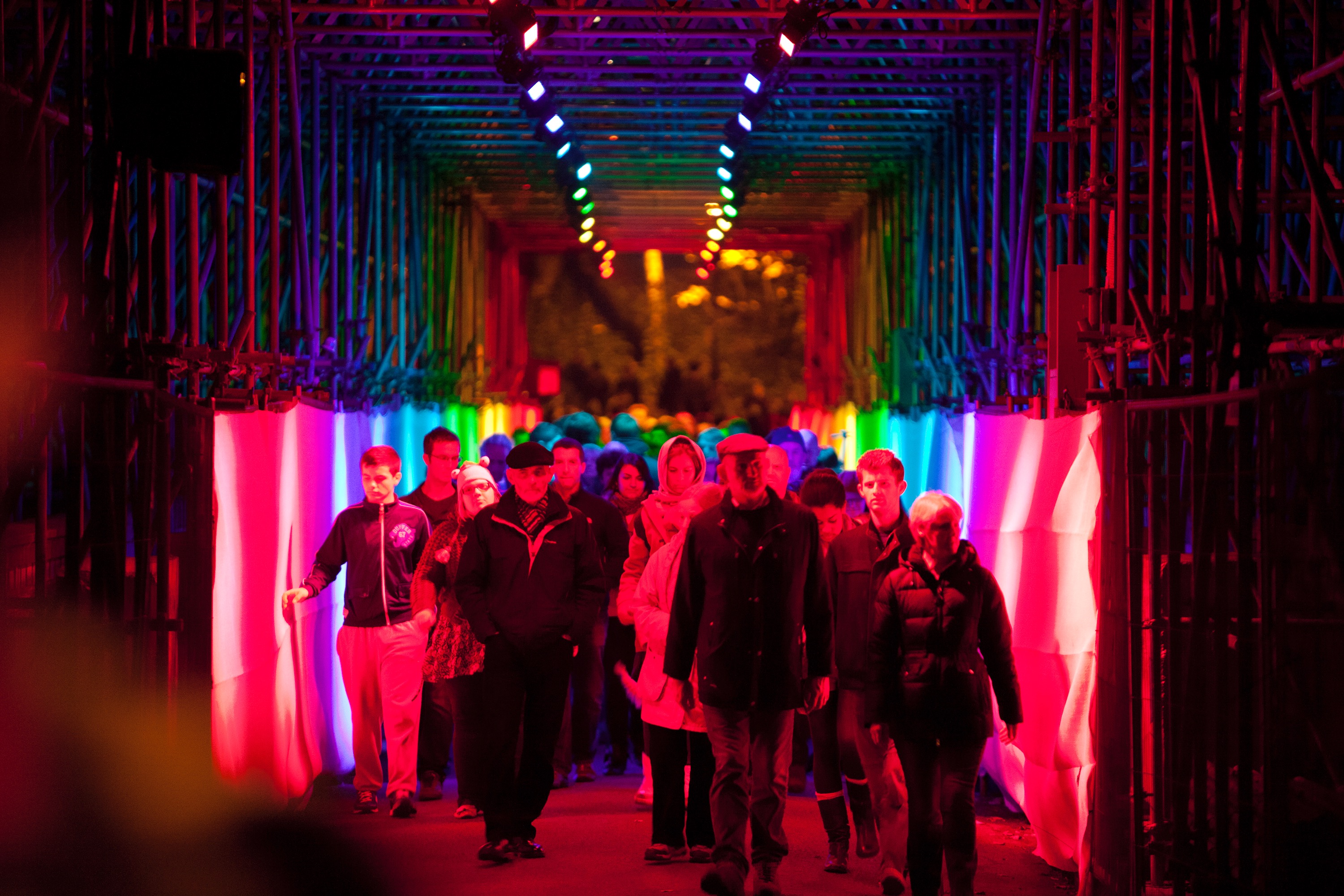 People walking through a square tunnel lit up in rainbow colours