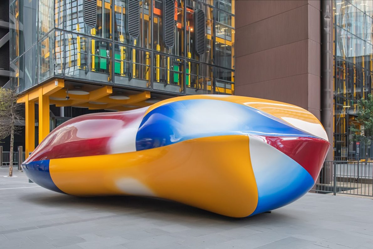 Colourful, abstract sculpture with smooth, rounded forms in red, blue, yellow, and white. It is situated outdoors behind the Cheesegrater in London