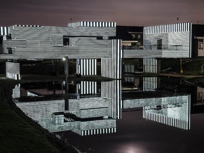 Apollo Pavilion illuminated at night via projection in striped monochrome light.