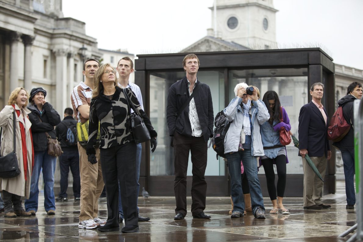 People of all different ages look up at the Fourth Plinth. Faces show a range of emotions from confusion to joy.