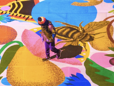 Child walking across multilcoloured floor projection with images of flowers, shapes, fruits and bees