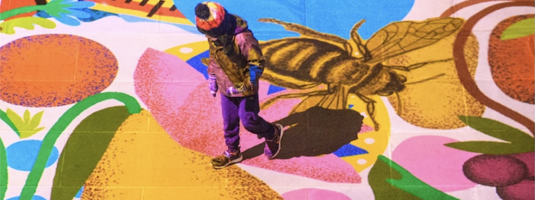 Child walking across multilcoloured floor projection with images of flowers, shapes, fruits and bees