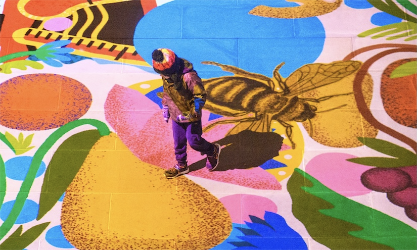 Child walking across multilcoloured floor projection with images of flowers, shapes, fruits and bees