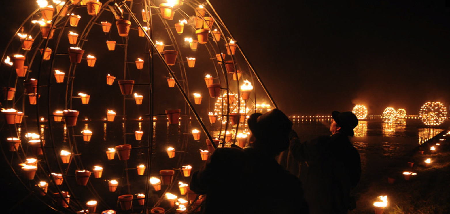 Two men in top hats with their performing as part of a fire installation on the river bank.