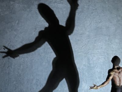 Man facing away and standing with his arms wide open - there is a giant shadow of him that is at the centre of the image