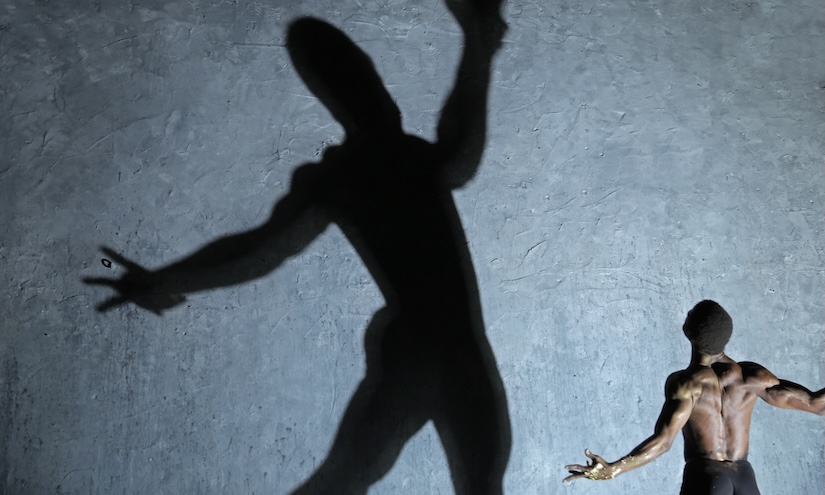Man facing away and standing with his arms wide open - there is a giant shadow of him that is at the centre of the image
