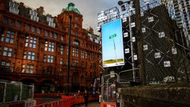 A billboard of the artwork ‘CRY’ (2022) by Allyson Packer on a busy London road. A barren landscape. A freight train can barely be seen in the distance. A road sign in the foreground reads 'CR Y'.