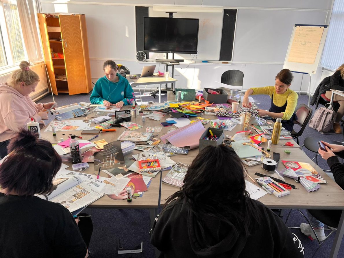 A workshop in Belfast for Season 2 of The Gallery. A group of young people sit in a room with piles of magazines on their work stations. They are creating collages in repsonse to the theme 