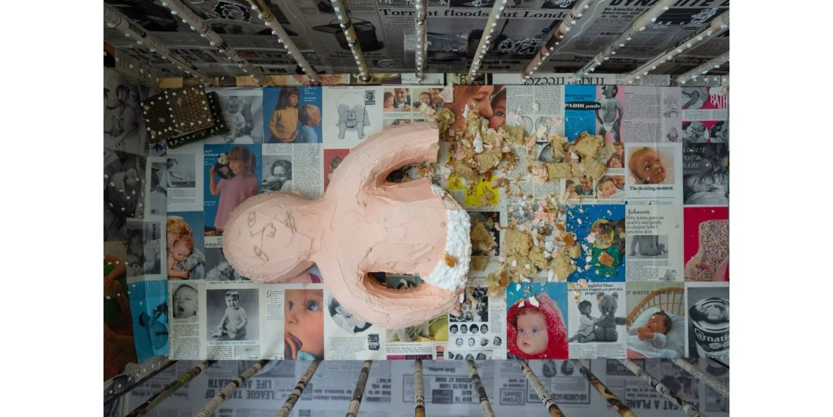 A top down view of a baby made of sponge cake whose legs have been eaten. The crib is plastered with images of babies from catalogues and magazines