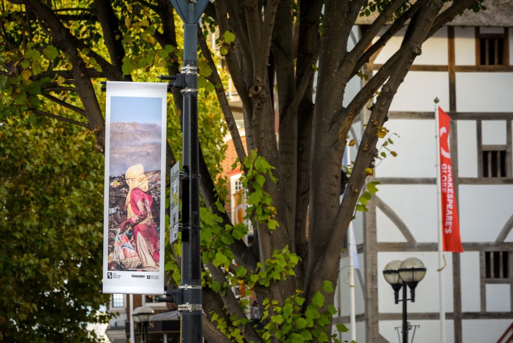 Outside Shakespeare's Globe, the artwork Grace on Waste where a girl collects recyclables in a landfill is displayed on a lampost.