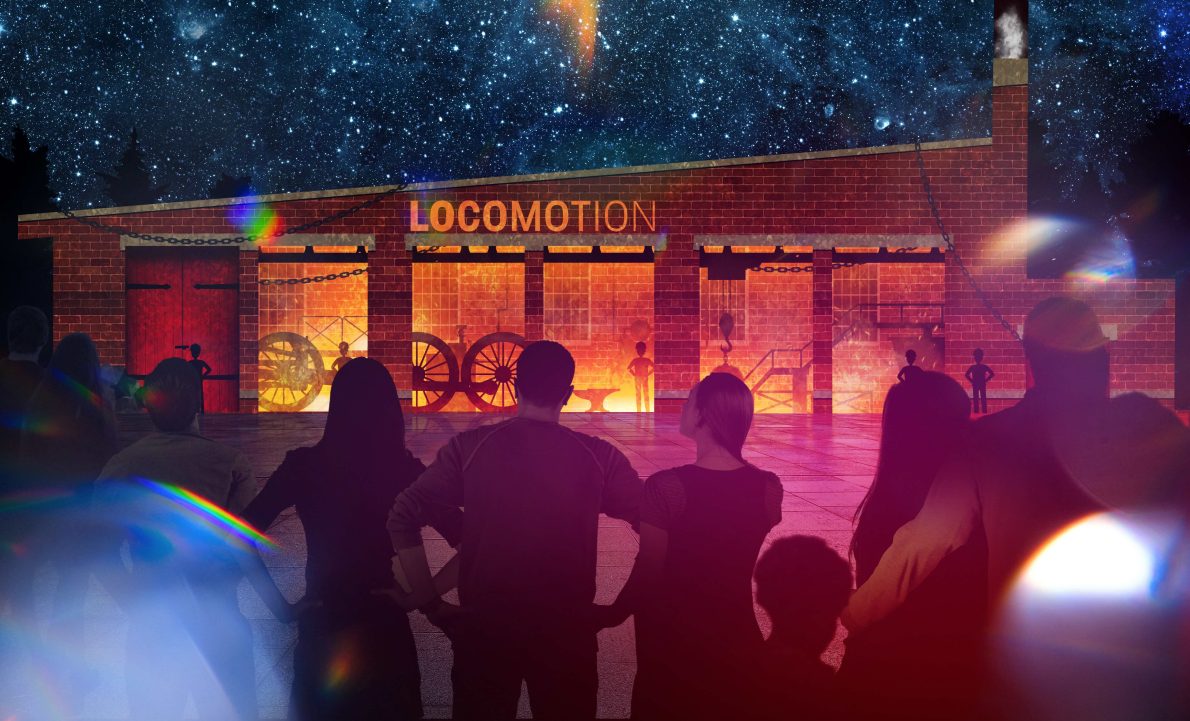 Night-time scene at the Locomotion museum in Shildon. A crowd of silhouetted visitors watches a vivid light projection on the museum’s brick building, showing glowing orange industrial interiors with wheels and workers under a starry sky.