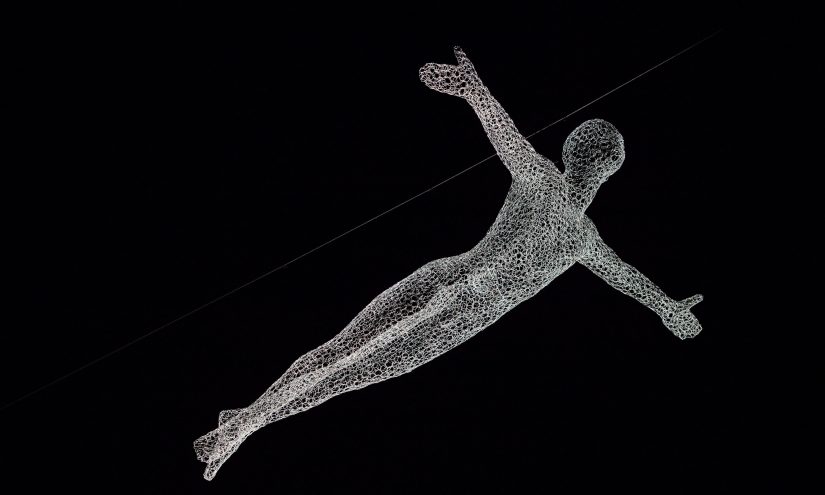A light art installation in the shape of a figure with their arms outstretched. The figure is made out of glowing mesh and appears to be flying through the night sky