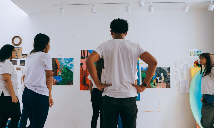Students in white t-shirts gaze upon a wall adorned with colourful artworks. The atmosphere is playful and creative