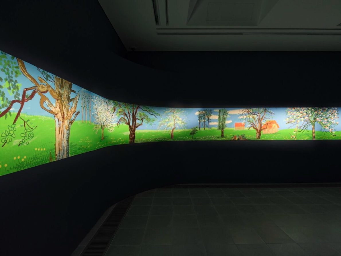 A brightly colored mural depicting a landscape with trees, green grass, and a blue sky on the walls of an art gallery.