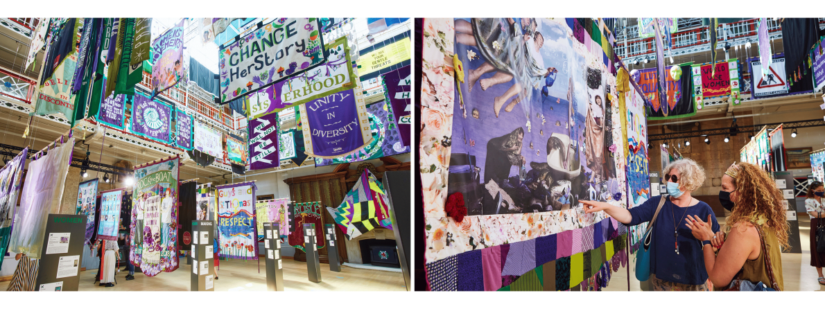 Exhibit featuring colourful, vibrant banners hanging at different levels with messages of change and unity. There are people discussing and pointing at the artwork.