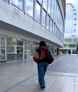 A person in a multicoloured jacket and jeans walks towards a photography exhibition on the side of the Royal Festival Hall in London, Southbank