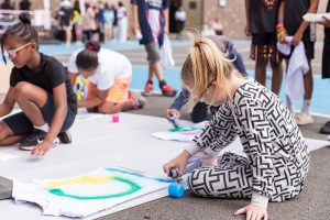 Children draw on large white pieces of paper on the floor using chalk.