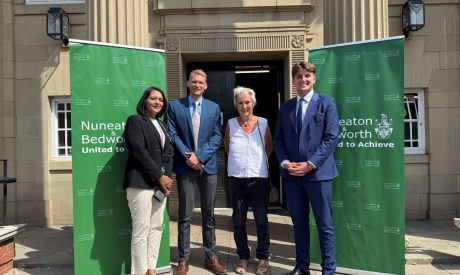 Four people stand outside the entrance of a civic building between two green Nuneaton & Bedworth Borough Council banners reading 