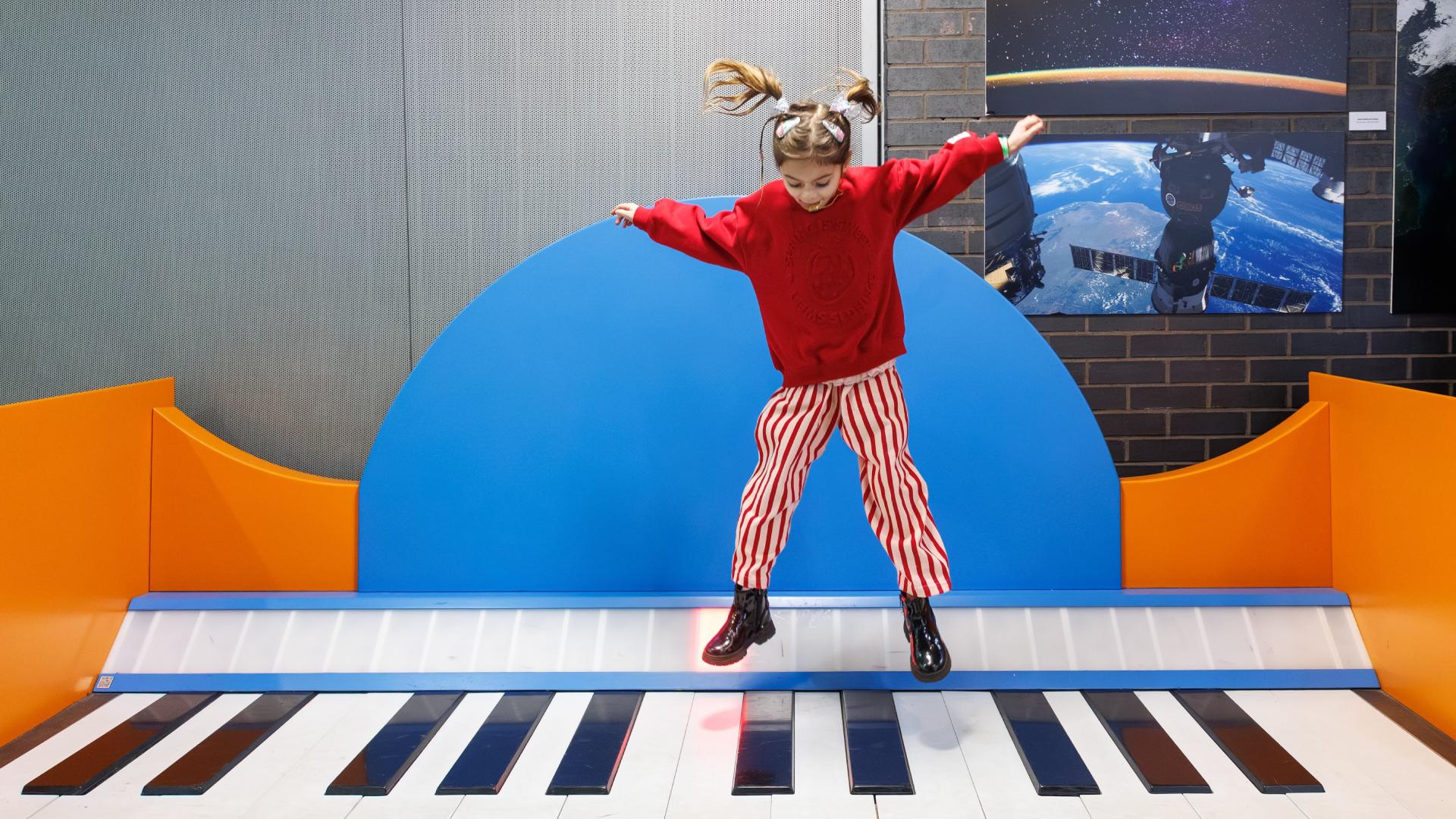 A young girl jumping in the air while playing a giant floor piano at Techniquest.