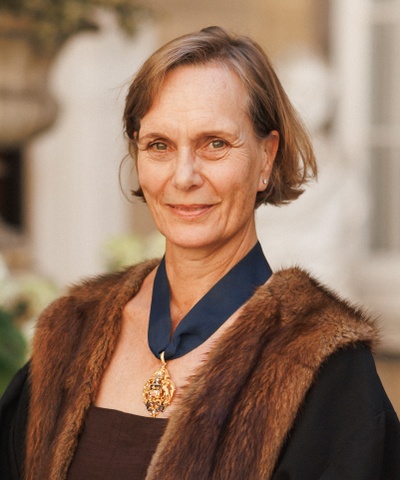 Mrs Hall looks into the camera, wearing a faux fur trimmed black robe and a badge of the MT crest around his neck