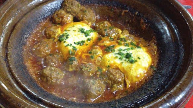 Meatballs sizzling in a tomato sauce, in a traditional Moroccan tagine dish (with two eggs on top).