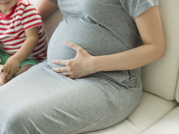 Pregnant woman sat on a sofa with her left hand on her stomach and her toddler son sat next to her