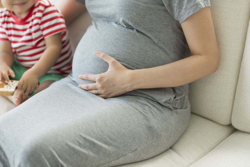 Pregnant woman sat on a sofa with her left hand on her stomach and her toddler son sat next to her