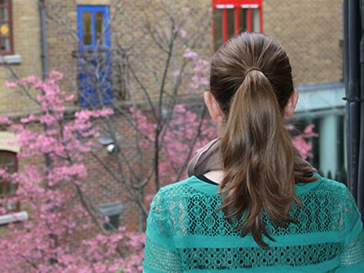 Woman facing away from the camera looking out of a window to a tree with pink leaves