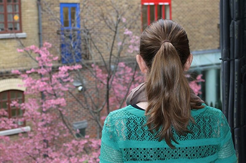 Woman facing away from the camera looking out of a window to a tree with pink leaves
