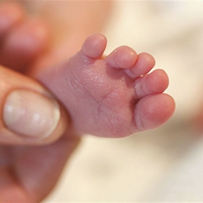 Baby's tiny foot being held by a parent's thumb and index fingers
