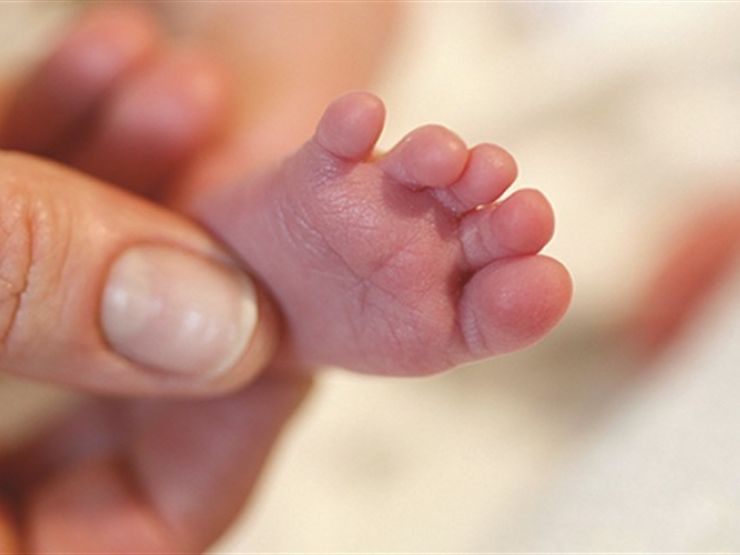 Baby's tiny foot being held by a parent's thumb and index fingers