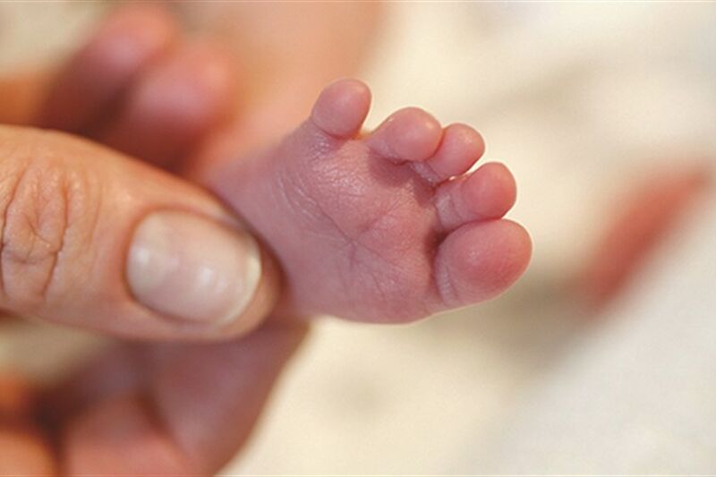 Baby's tiny foot being held by a parent's thumb and index fingers