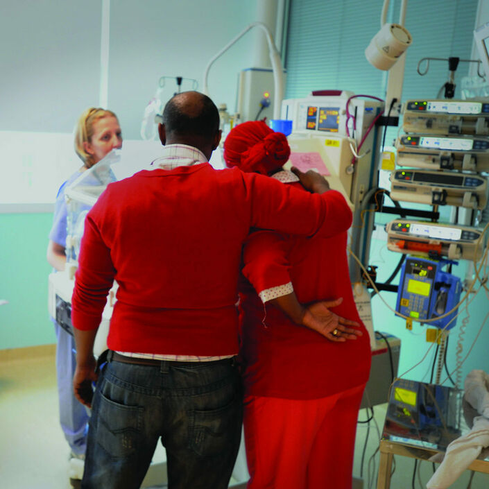 Parents standing over their baby's cot with their arms round each other