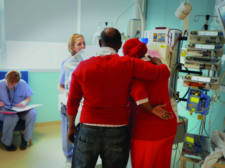 Parents standing over their baby's cot with their arms round each other