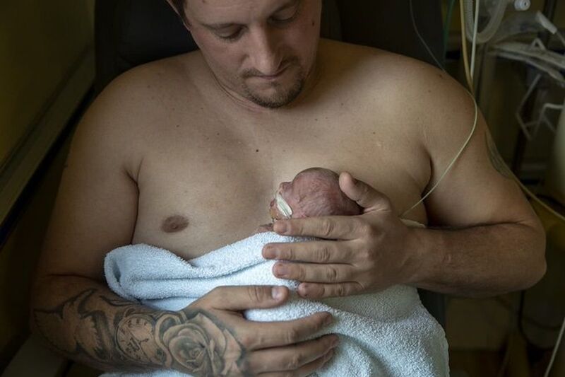 Dad holding his baby against his chest skin to skin while looking down at baby