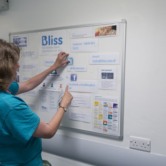 Woman with Bliss t-shirt looking at a notice board in a hospital setting