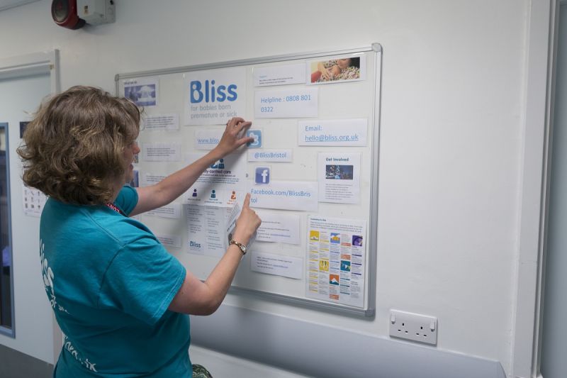 Woman with Bliss t-shirt looking at a notice board in a hospital setting