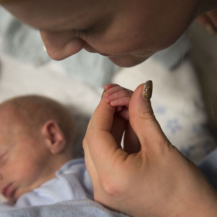 Baby asleep while mum holds his hand in hers